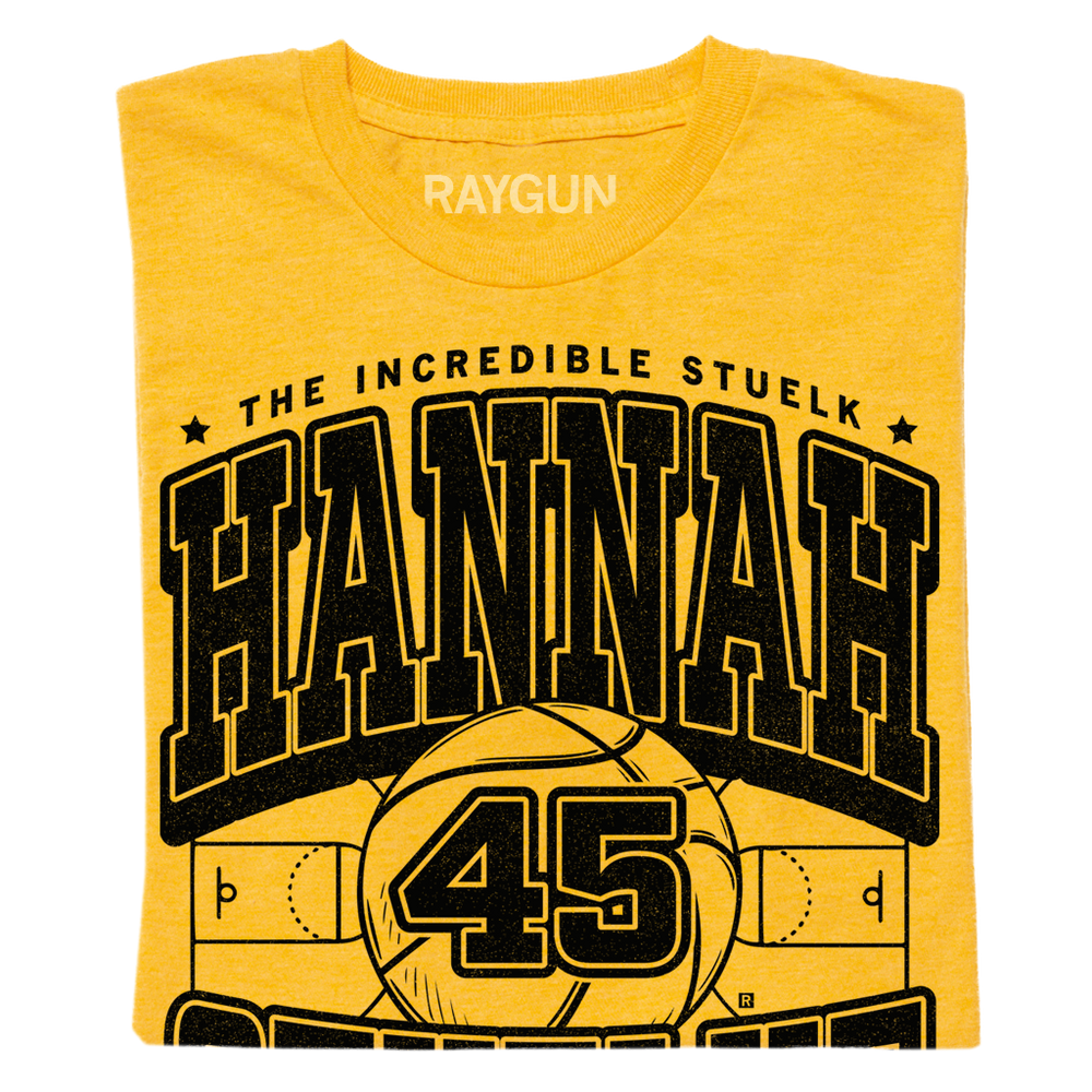 a folded gold shirt with black print that says, "The Incredible Stuelk. Hannah Stuelke. Forward. Cedar Rapids" over an illustration of a giant basketball and a basketball court.