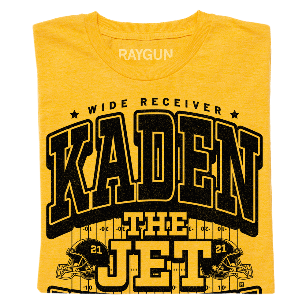 A folded yellow shirt with black text that says, "Wide Receiver Kaden the Jet Wetjen. Willamsburg, IA" over an illustration of a football field and two footballs helmets facing either side with the number 21 on them.