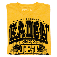 A folded yellow shirt with black text that says, "Wide Receiver Kaden the Jet Wetjen. Willamsburg, IA" over an illustration of a football field and two footballs helmets facing either side with the number 21 on them.