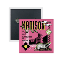 A pink square metal button in a retro 90's style with a black print image of the Wisconsin Capitol building in Madison. Black text  across the tops says, "Madison" with more text to the left that reads, "77 sq. miles surrounded by reality." There's also a black and white badger, green squiggle, white clouds, and other colorful accents.