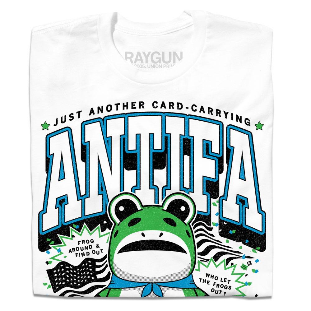 Folded white t-shirt with the text "Just another card-carrying ANTIFA member" above and below an illustration of the Portland protestor in a frog suit. To the sides are an American flag and the text "Frog around & find out. Who let the frogs out?"