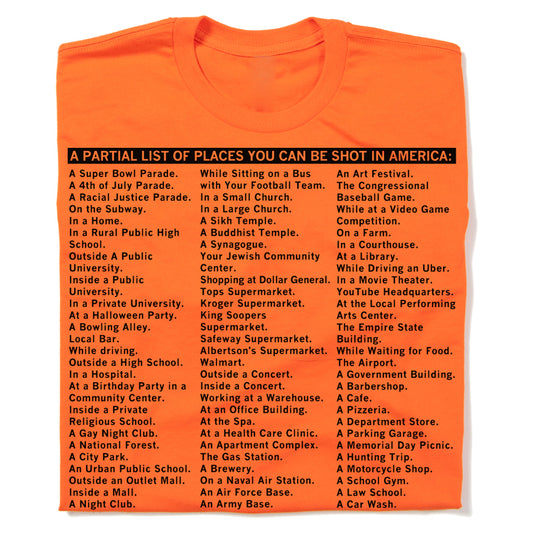Bright orange RAYGUN t-shirt printed with black text titled A PARTIAL LIST OF PLACES YOU CAN BE SHOT IN AMERICA, followed by a list of locations ranging from schools and grocery stores to parks and religious centers.