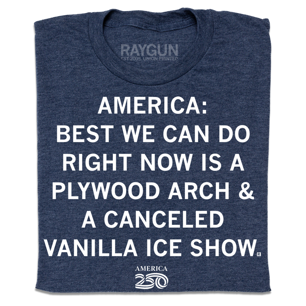 A folded heather navy t-shirt with centered white ink text that reads "America 250: best we can do right now is a plywood arch &amp; a canceled Vanilla Ice show."
