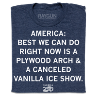 A folded heather navy t-shirt with centered white ink text that reads "America 250: best we can do right now is a plywood arch &amp; a canceled Vanilla Ice show."