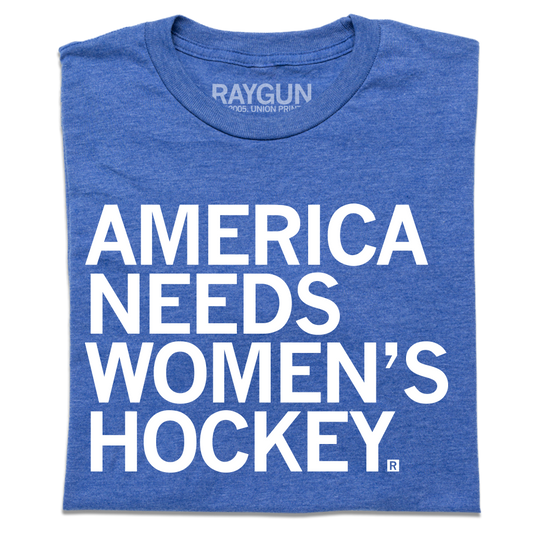 A folded heather royal blue t-shirt with left-aligned white ink text that reads "America Needs Women's Hockey"