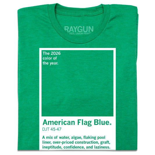 A folded heather kelly green t-shirt with white ink printed to look like a pantone color that says, "The 2026 color of the year: American Flag Blue. A mix of water, algae, flaking pool liner, over-priced construction, graft, ineptitude, confidence, and laziness."
