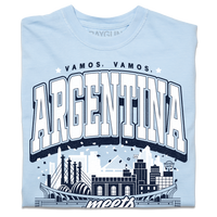 A light blue heavyweight t-shirt with navy and white ink. From the top to the bottom the text reads "Vamos, Vamos, Argentina meets Kansas City. World Cup 2026, Missouri." In the center is an illustration depicting notable buildings from Argentina and Kansas City mixed together.
