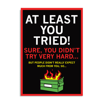 Black postcard with white, red, and gold text that says "At Least You Tried! Sure, you didn't try very hard... But people didn't really expect much from you, so..." over a dumpster fire