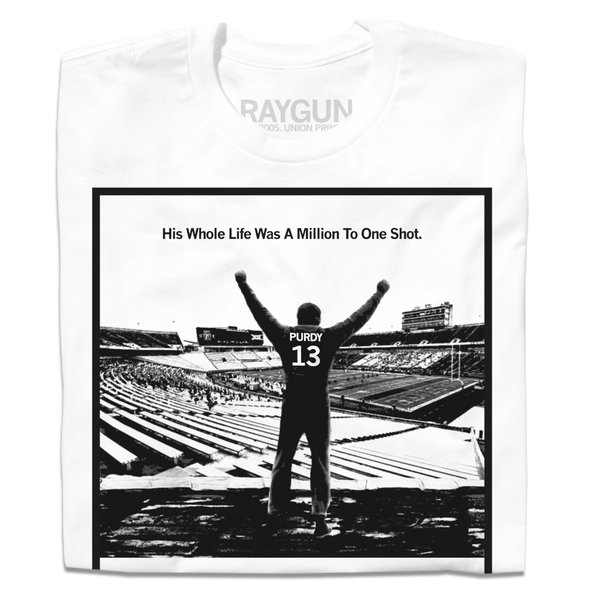 A folded white t-shirt with a black ink image spoofing Rocky, depicting Brock Purdy looking over his old college stadium. Above him with his fists raised in the air is the text 