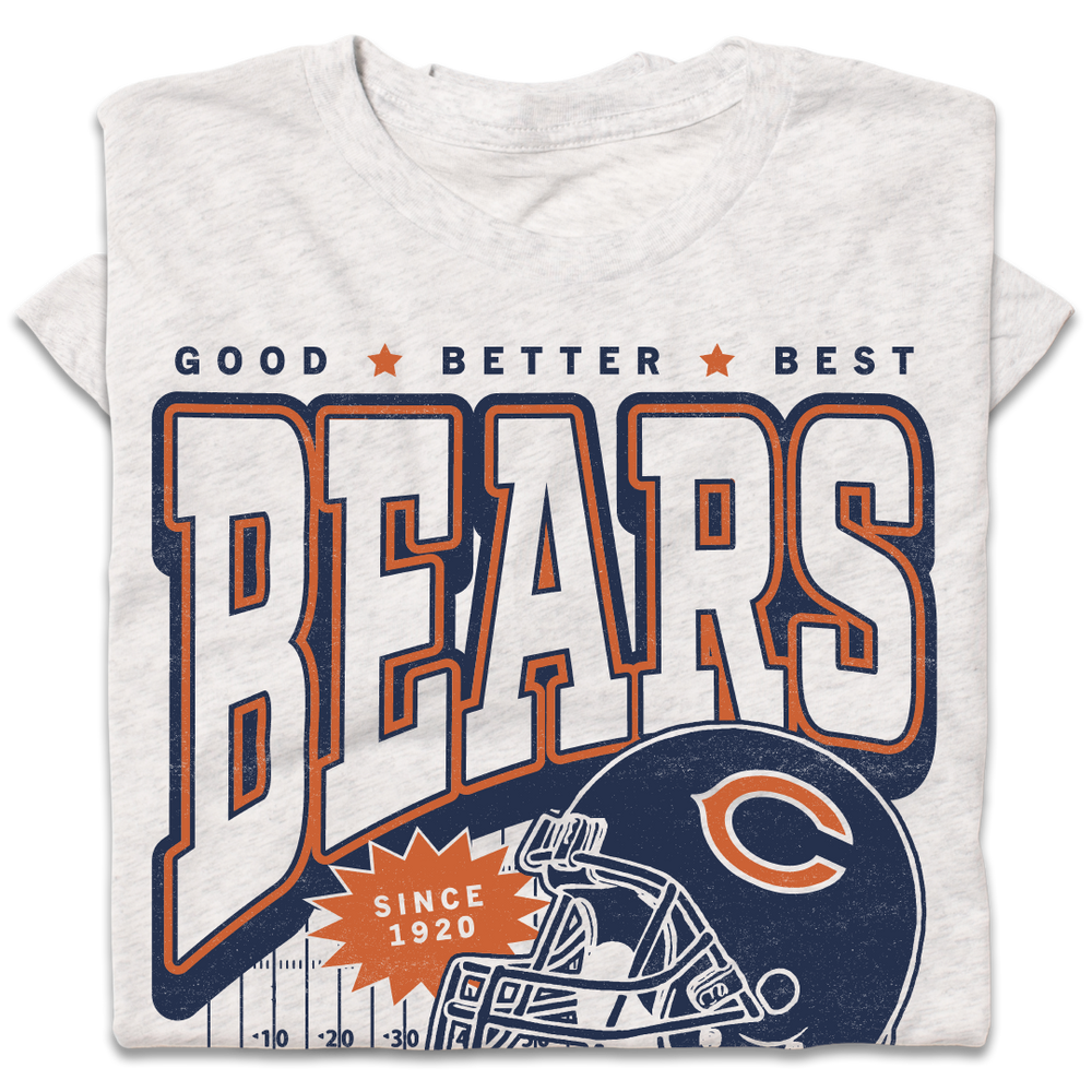 A folded heather white t-shirt with a vintage style print in orange and navy ink. Text from top to bottom reads "Good, Better, Best. Bears. Since 1920. Chicago. Pope Approved." There's a football helmet over a football field in the center.