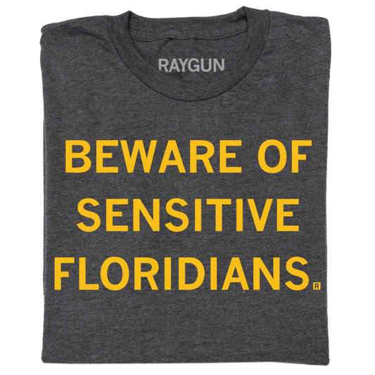 A folded charcoal t-shirt with centered gold ink text that reads "Beware of sensitive Floridians"