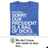 A funny political RAYGUN t-shirt in blue with white text that reads: DEAR WORLD, SORRY OUR PRESIDENT IS A BAG OF DICKS. SINCERELY, HALF OF USA.