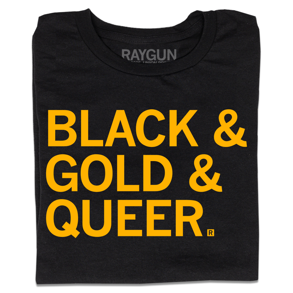 A folded black t-shirt with large, left-aligned gold text that reads "Black & Gold & Queer"