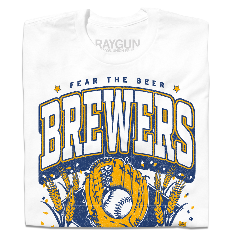 A folded white t-shirt with gold and blue ink that reads "Fear the beer. Milwaukee Brewers. American Family Field." with a baseball landing in a mitt in the center and beer hops growing on either side.