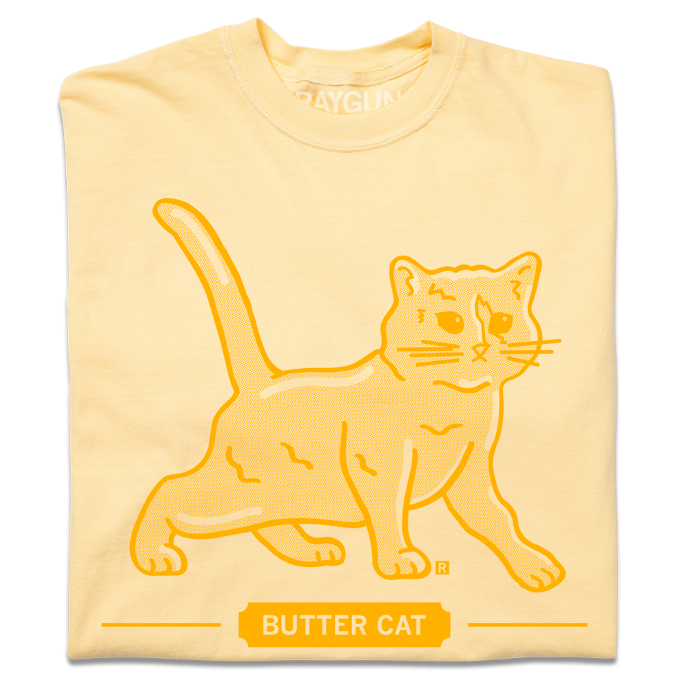 A folded pastel yellow t-shirt with gold ink printed  a gradient depicting a cat made of butter. Text below says, "BUTTER CAT."