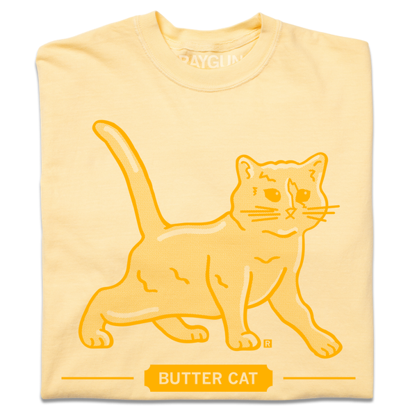 A folded pastel yellow t-shirt with gold ink printed  a gradient depicting a cat made of butter. Text below says, 