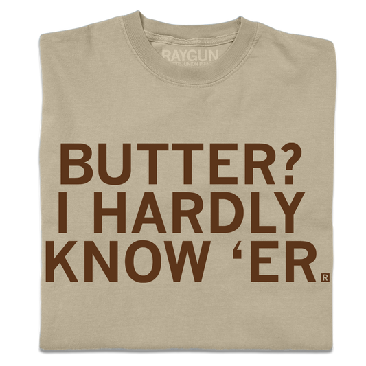 A folded khaki t-shirt with centered brown ink text that says, "Butter? I hardly know 'er" in all caps.