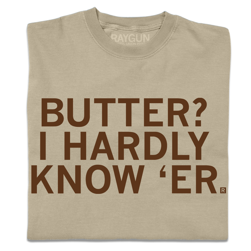 A folded khaki t-shirt with centered brown ink text that says, "Butter? I hardly know 'er" in all caps.