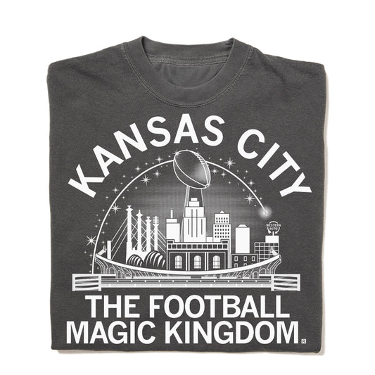 Dark gray RAYGUN t-shirt featuring a white graphic of the Kansas City skyline, a football trophy, and the text Kansas City The Football Magic Kingdom.