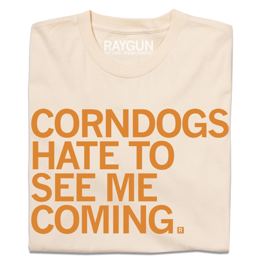 Cream-colored, union-made t-shirt with the text CORNDOGS HATE TO SEE ME COMING printed in orange.