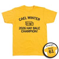 Short-sleeve heather mellow yellow t-shirt with a black print image of a hay bale with an outline of Iowa on it and number 61 in the center. Curved text at the top says, "CAEL WINTER" and straight text below reads "2026 HAY BALE CHAMPION." A small circle image in the bottom right highlights the back print. The back of the shirt is laid out like a jersey with "WINTER" printed above "61"