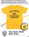 Heather Mellow Yellow t-shirt printed with Cael Winter 2026 Hay Bale Champion! and an illustration of a hay bale, with an inset showing the back of the shirt reading Winter 61.