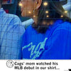 A woman wearing a RAYGUN shirt with white lettering watches a game from behind a protective net.