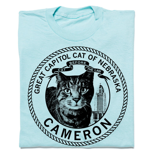 Light blue RAYGUN t-shirt featuring a circular graphic of a cat, the Nebraska State Capitol, and the text Great Capitol Cat of Nebraska: Cameron: Before the Law.