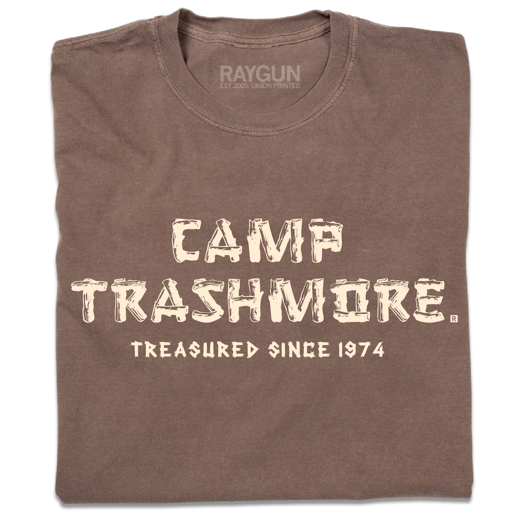 A folded brown heavyweight t-shirt with off-white ink that says, "Camp Trashmore. Treasured since 1974." printed in a font reminiscent of old summer camps.