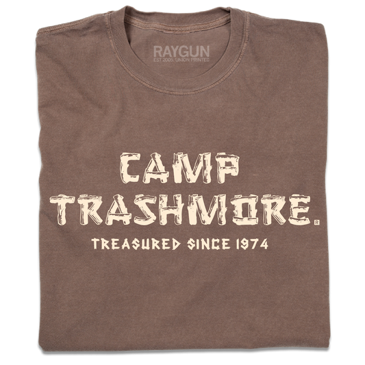 A folded brown heavyweight t-shirt with off-white ink that says, "Camp Trashmore. Treasured since 1974." printed in a font reminiscent of old summer camps.