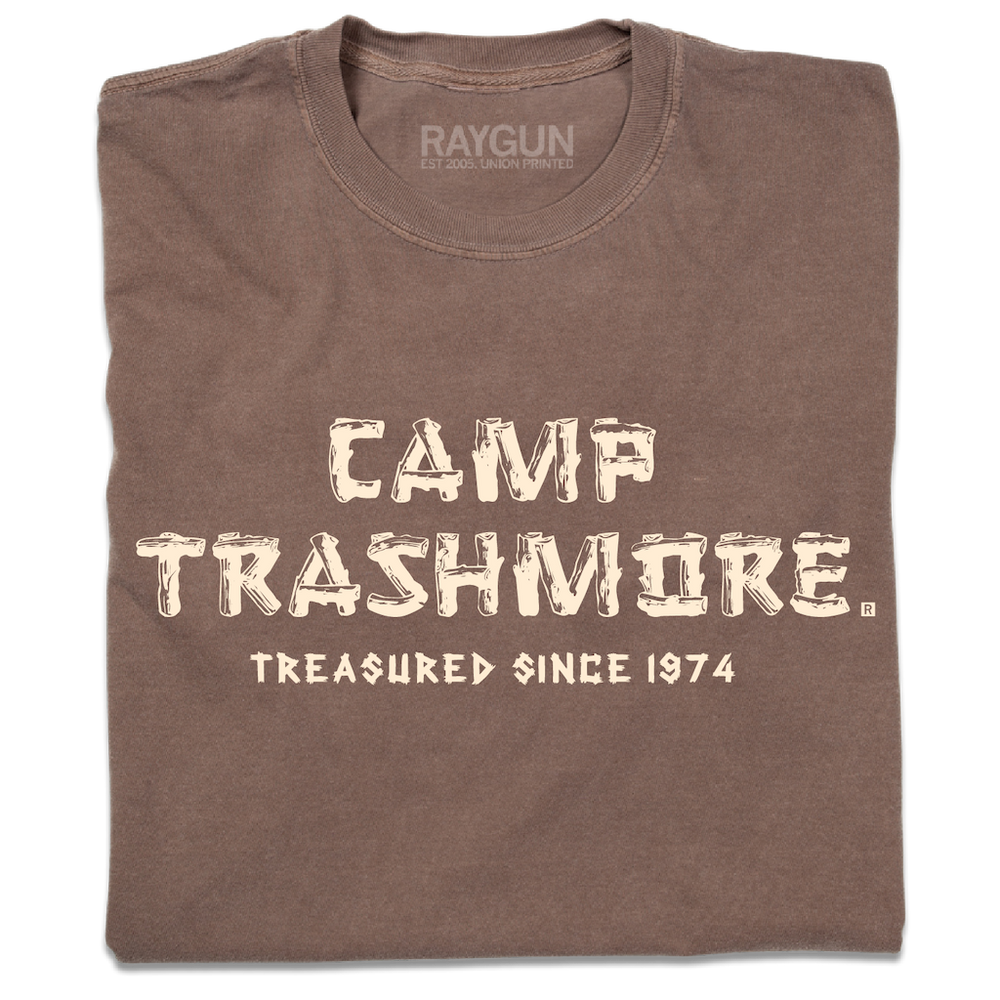 A folded brown heavyweight t-shirt with off-white ink that says, "Camp Trashmore. Treasured since 1974." printed in a font reminiscent of old summer camps.