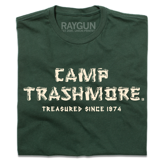 A folded forest green t-shirt with off-white ink that says, "Camp Trashmore. Treasured since 1974." printed in a font reminiscent of old summer camps.