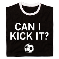 A folded black ringer shirt with a white neckline and sleeves. Centered white ink text reads can I kick it?" above an illustration of a soccer ball.