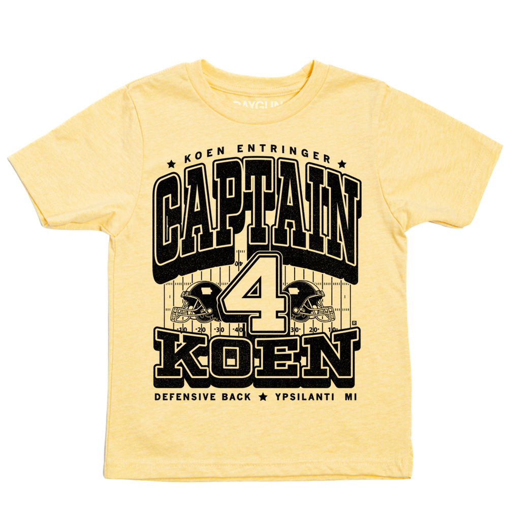 Pastel yellow youht t-shirt with black ink that reads "Koen Entrigner. Captain Koen. Defensive Back. Ypsilanti, MI" over an illustration of a football field with a large number 4 in the center and a football helmet to either side.