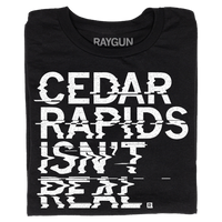 A folded black t-shirt with left-aligned white ink text printed in a distorted style that reads "Cedar Rapids Isn't Real"