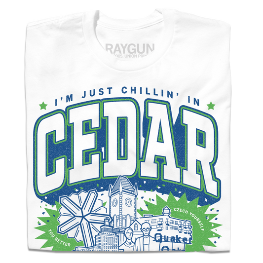 White screen print T-shirt featuring a graphic that says IM JUST CHILLIN IN CEDAR above Cedar Rapids landmarks, including a clock tower and a windmill, with the text YOU BETTER CZECH YOURSELF and Quaker at the bottom.