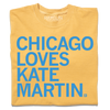 A folded heavyweight mustard t-shirt with left-aligned bright blue text that reads "CHICAGO LOVES KATE MARTIN."