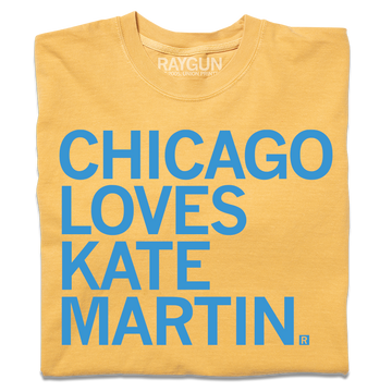 A folded heavyweight mustard t-shirt with left-aligned bright blue text that reads "CHICAGO LOVES KATE MARTIN."