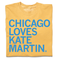A folded heavyweight mustard t-shirt with left-aligned bright blue text that reads "CHICAGO LOVES KATE MARTIN."