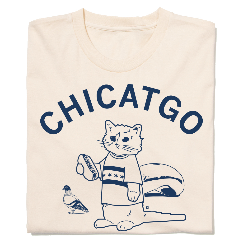 A folded off-white t-shirt with curved navy ink that reads "Chicatgo" over an illustration of RAYGUN's cat mascot wearing a Chicago flag t-shirt while holding a hotdog. The Bean is behind him and there's a pigeon beside him.