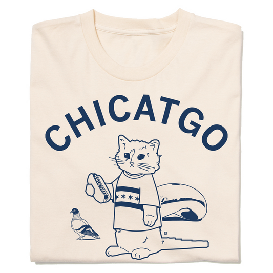 A folded off-white t-shirt with curved navy ink that reads "Chicatgo" over an illustration of RAYGUN's cat mascot wearing a Chicago flag t-shirt while holding a hotdog. The Bean is behind him and there's a pigeon beside him.