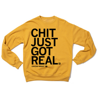 A folded heather mustard crewneck sweatshirt with left aligned black ink that reads "Chit Just Got Real. Chazadi Wright 11"