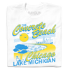 A folded white shirt with bright yellow and blue print that reads "The Concrete Beach. Chicago, Lake Michigan" with an illustration of a beachfront Chicago skyline and a pigeon in the corner.