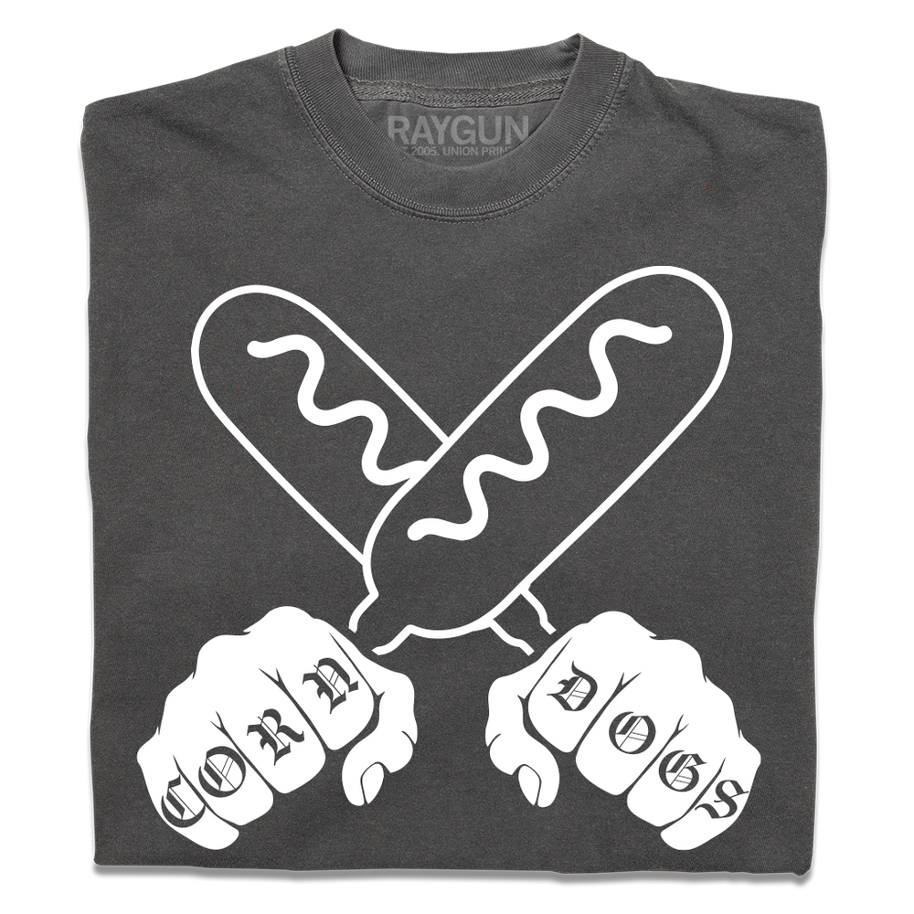 A folded grey t-shirt with a white print illustration of two hands holding corndogs in an X shape with knuckle tattoos that spell out "CORNDOGS."