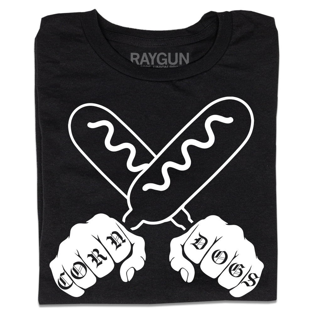 A folded black t-shirt with a white print illustration of two hands holding corndogs in an X shape with knuckle tattoos that spell out "CORNDOGS."