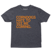A youth size heather black t-shirt with orange print text that says, "CORNDOGS HATE TO SEE ME COMING"