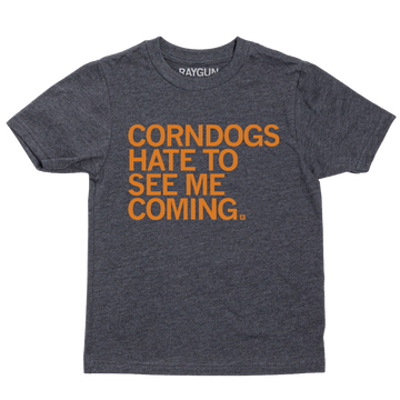 A youth size heather black t-shirt with orange print text that says, "CORNDOGS HATE TO SEE ME COMING"