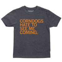 A youth size heather black t-shirt with orange print text that says, "CORNDOGS HATE TO SEE ME COMING"