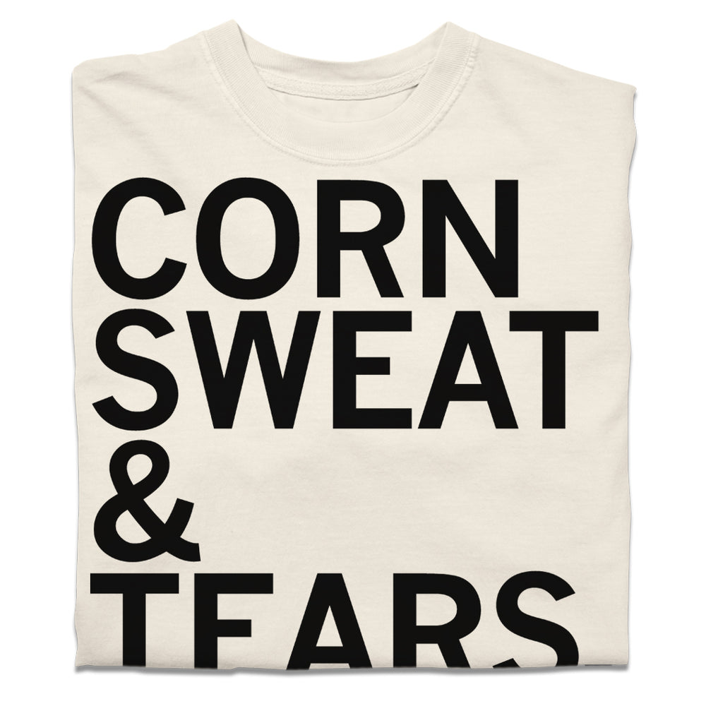 A folded off-white t-shirt with black text that says, "corn sweat & tears."