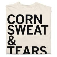 A folded off-white t-shirt with black text that says, "corn sweat & tears."
